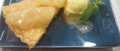 Un piatto dessert con una fetta di torta rovesciata all'ananas e una pallina di gelato alla vaniglia, guarnito con una fogliolina di menta.