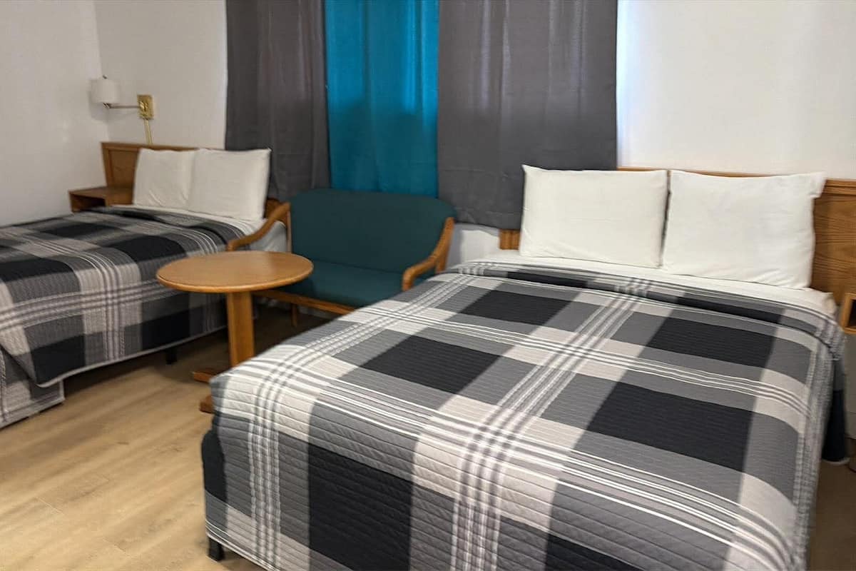 A hotel room with two beds, a small round table, a chair, and a window with curtains.