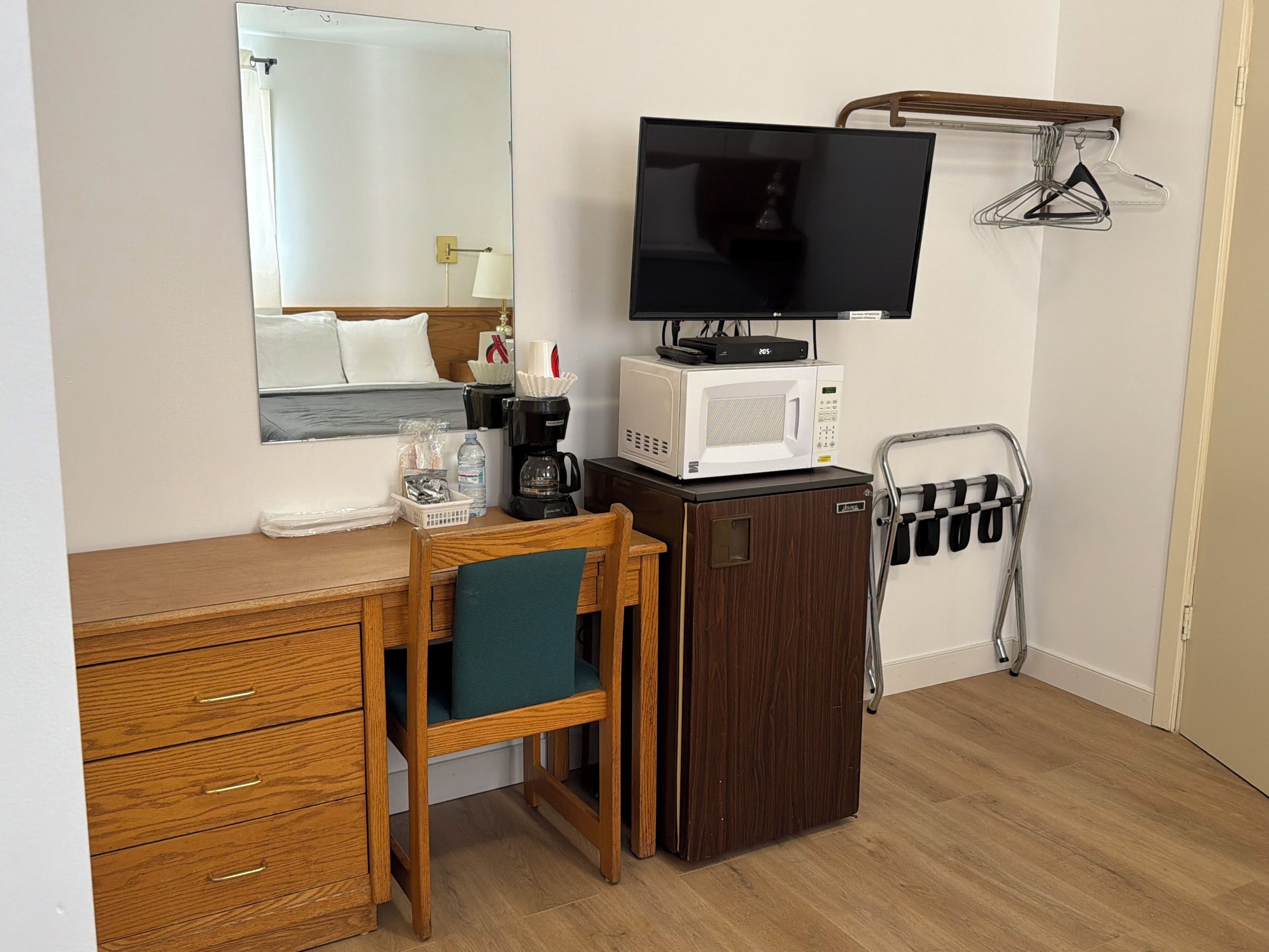 A small room with a wooden desk, a chair, a television, a microwave, a coffee maker, and a clothes drying rack.