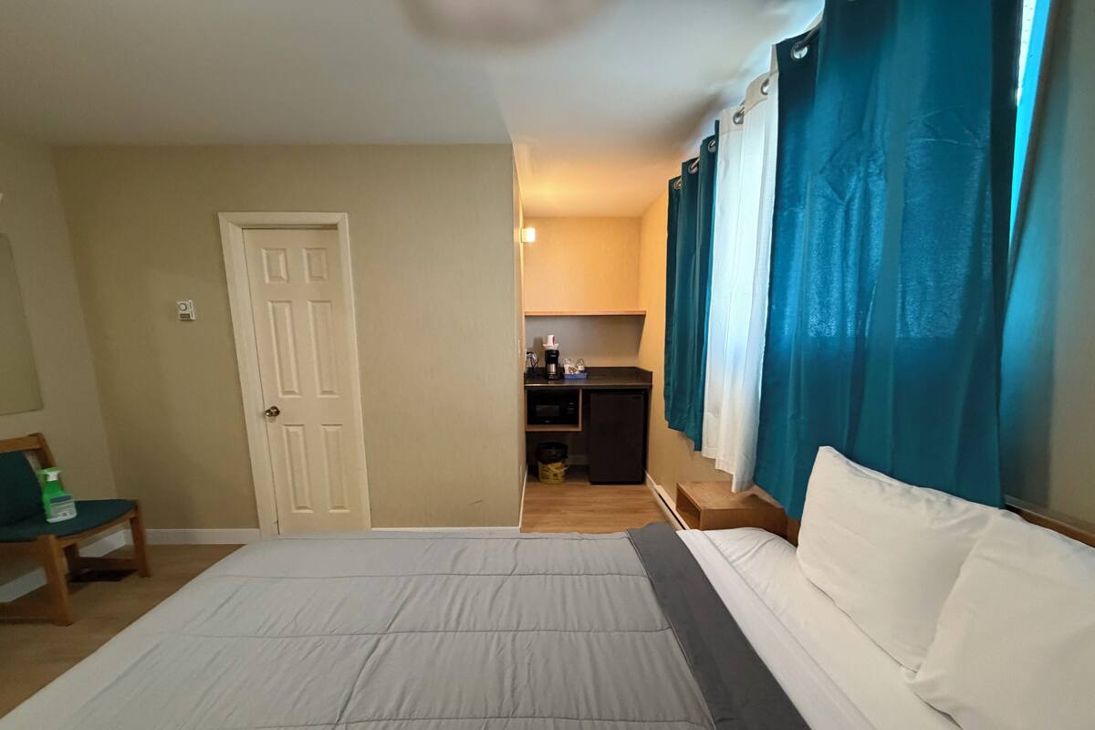 A hotel room with a bed, a desk, a chair, and a kitchenette.