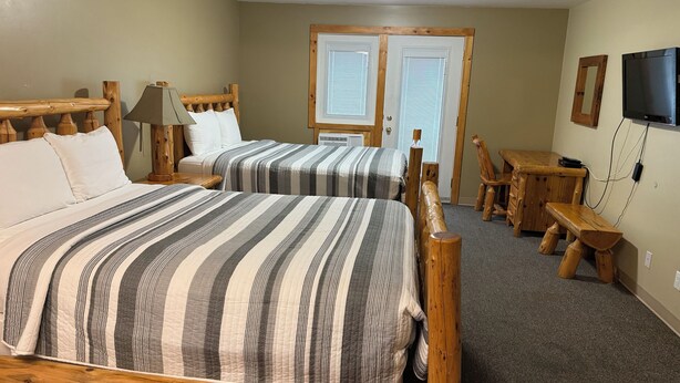 A room with two beds, a wooden headboard, a desk, a chair, a television, and a door with windows. - Lake-Vu Motel (Kenora)