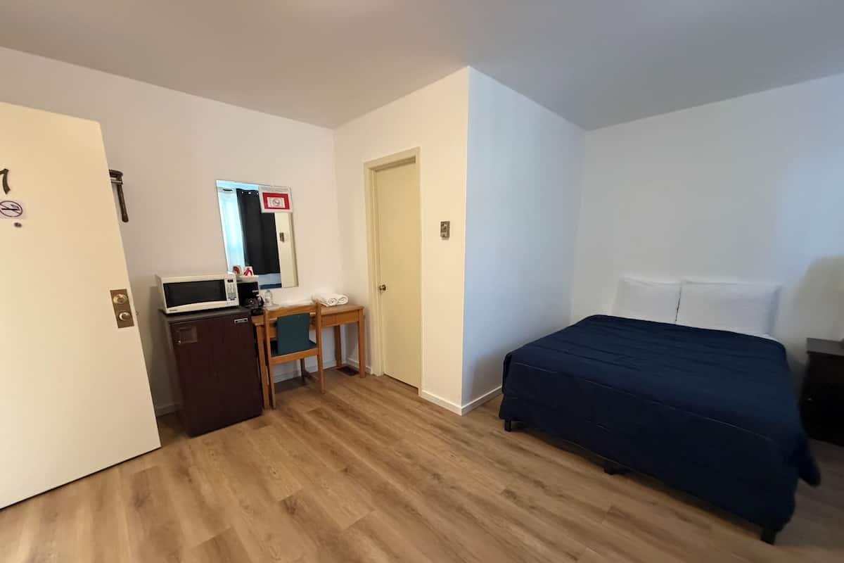 A hotel room with a bed, a desk with a chair, a microwave, and a small refrigerator.