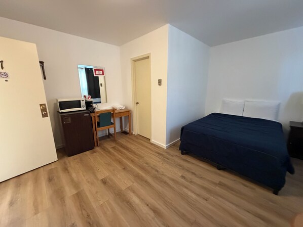 Una habitación de hotel con una cama, un escritorio con una silla, un microondas y un refrigerador pequeño.