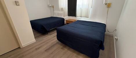 Et værelse med to senge, et vindue med gardiner, et sengebord og en væglampe.