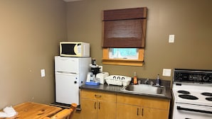 A compact kitchen with a refrigerator, microwave, stove, and wooden cabinets. - Lake-Vu Motel (Kenora)