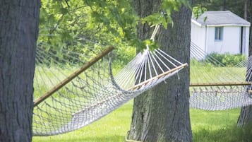 A hammock tied between two trees in a grassy area with a small white building in the background.