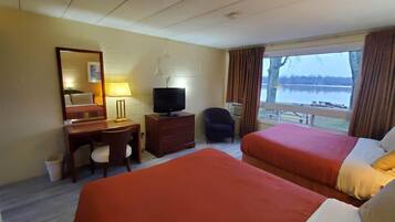 A hotel room with two beds, a desk with a chair, a television, a lamp, and a window with a view of a lake.