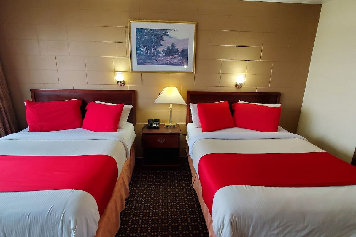 A hotel room with two beds, each with red and white bedding, a nightstand with a lamp, and a framed picture on the wall.