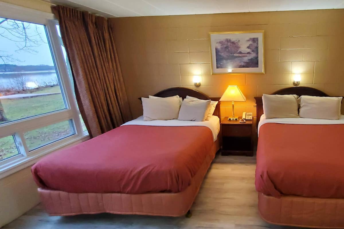 A hotel room with two beds, a nightstand with a lamp, a painting on the wall, and a window with curtains.
