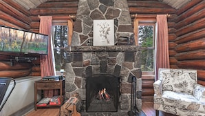 A log cabin interior with a stone fireplace, a television, a sofa, and a fireplace screen. - Cascade Lodge (Lutsen)