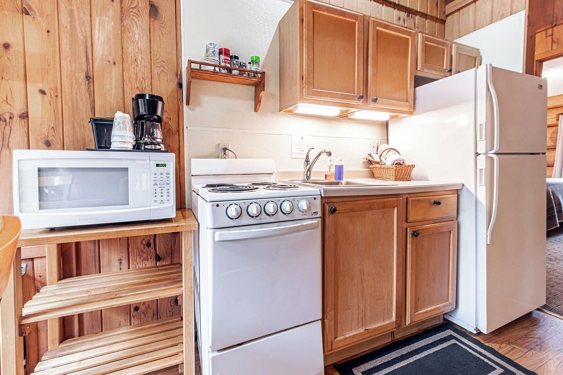 A compact kitchen with wooden cabinets, a white stove, a microwave, and a refrigerator.