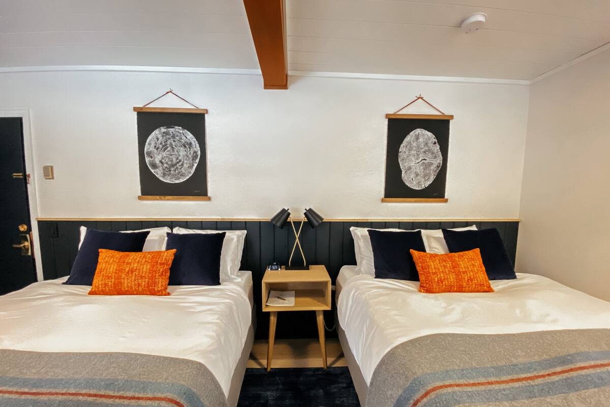 A hotel room with two beds, each with white linens and orange pillows. There are two framed artworks on the wall above the beds.