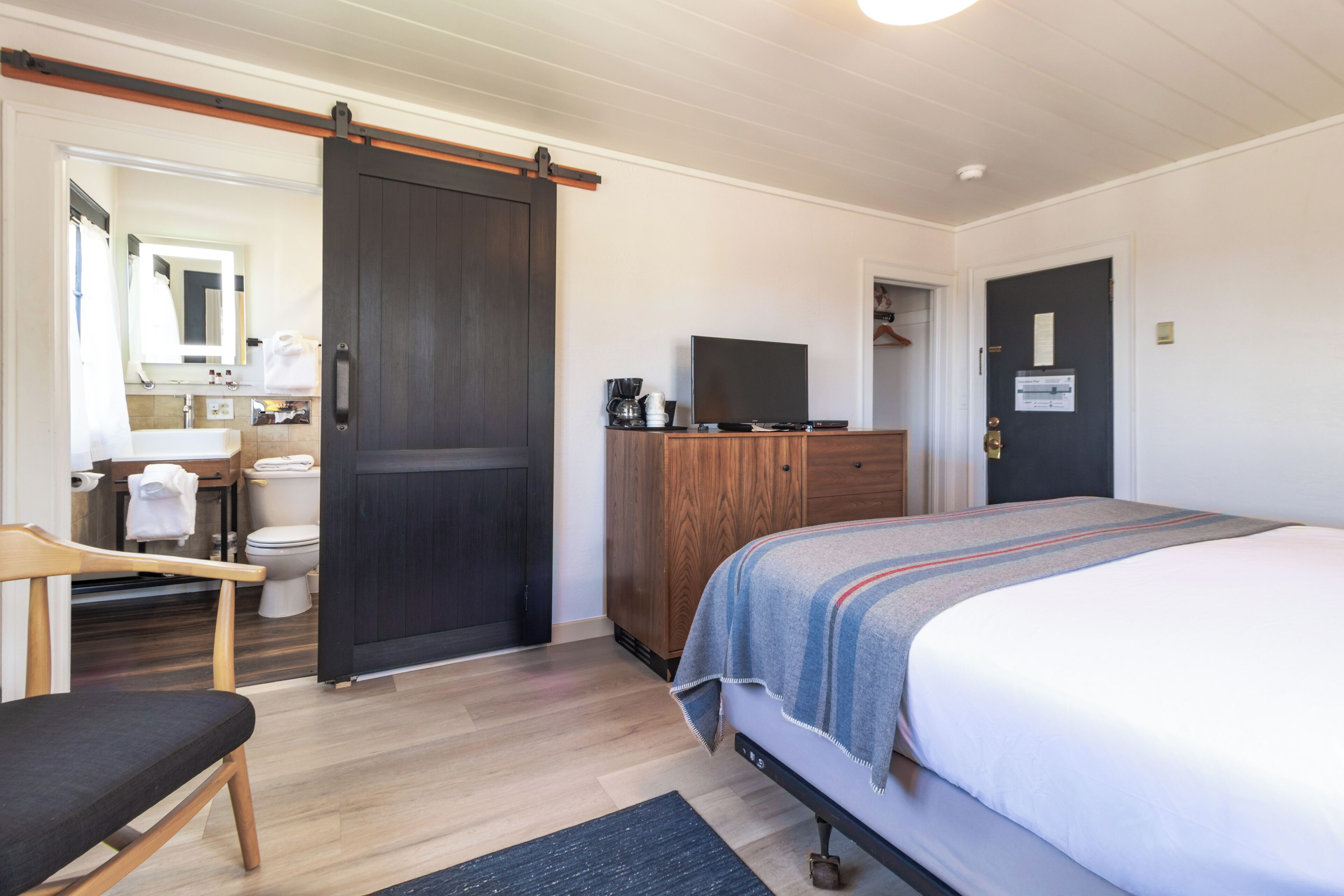 Un dormitorio con una cama, un armario de madera, una televisión y un baño a la vista a través de una puerta abierta.