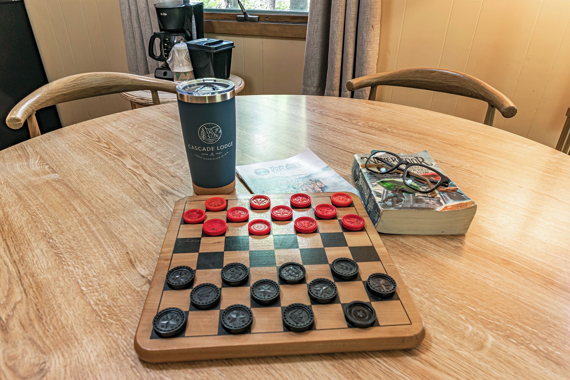 A wooden table with a chessboard, a coffee cup, and a box of chess pieces.