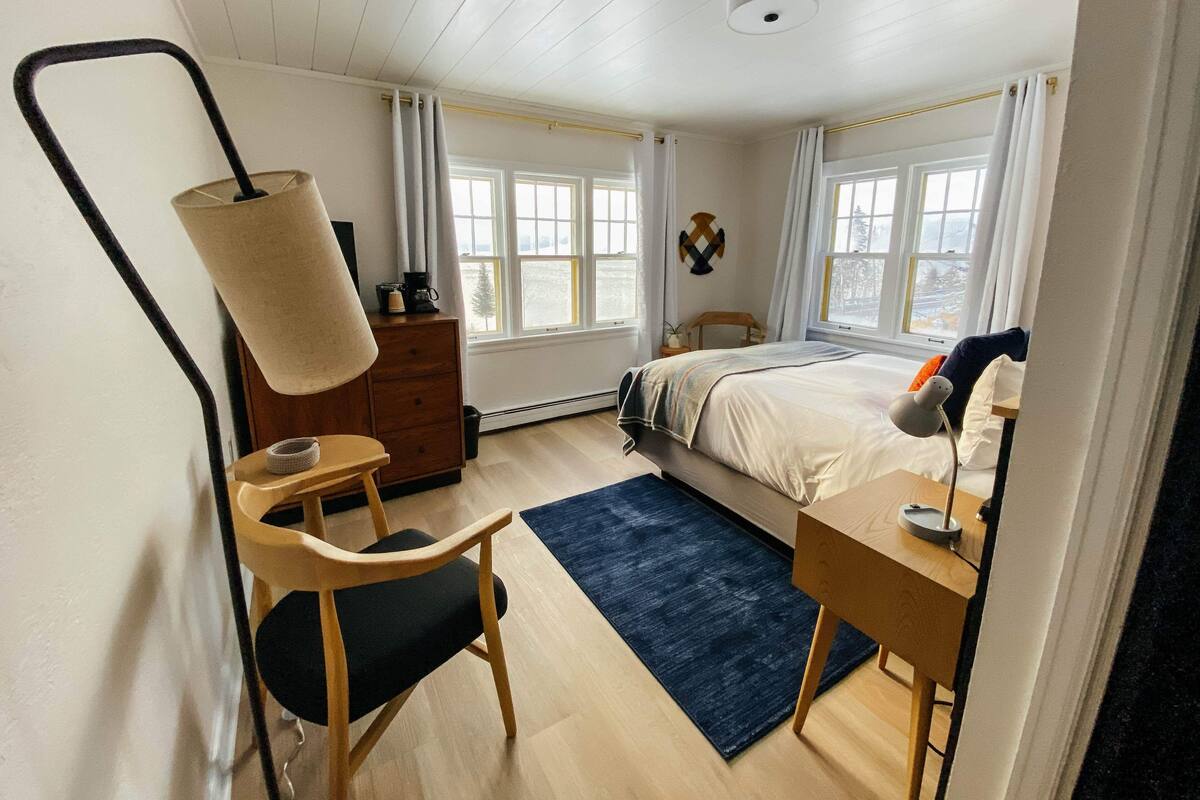A bedroom with a bed, a desk, a chair, a lamp, and a window.