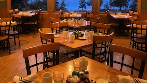 A restaurant with wooden interiors, tables set for dining, and large windows offering a view of trees and mountains. - Cascade Lodge (Lutsen)