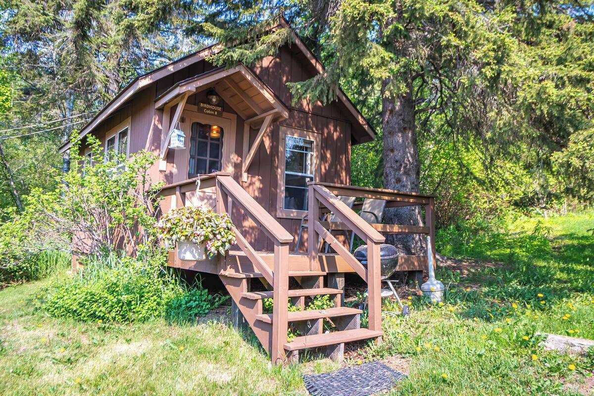 A cabin with a wooden staircase leading to a porch, surrounded by greenery.