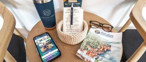 Una mesa de madera con un teléfono inteligente, una guía de viaje, una tarjeta de agradecimiento, un vaso y un par de gafas.