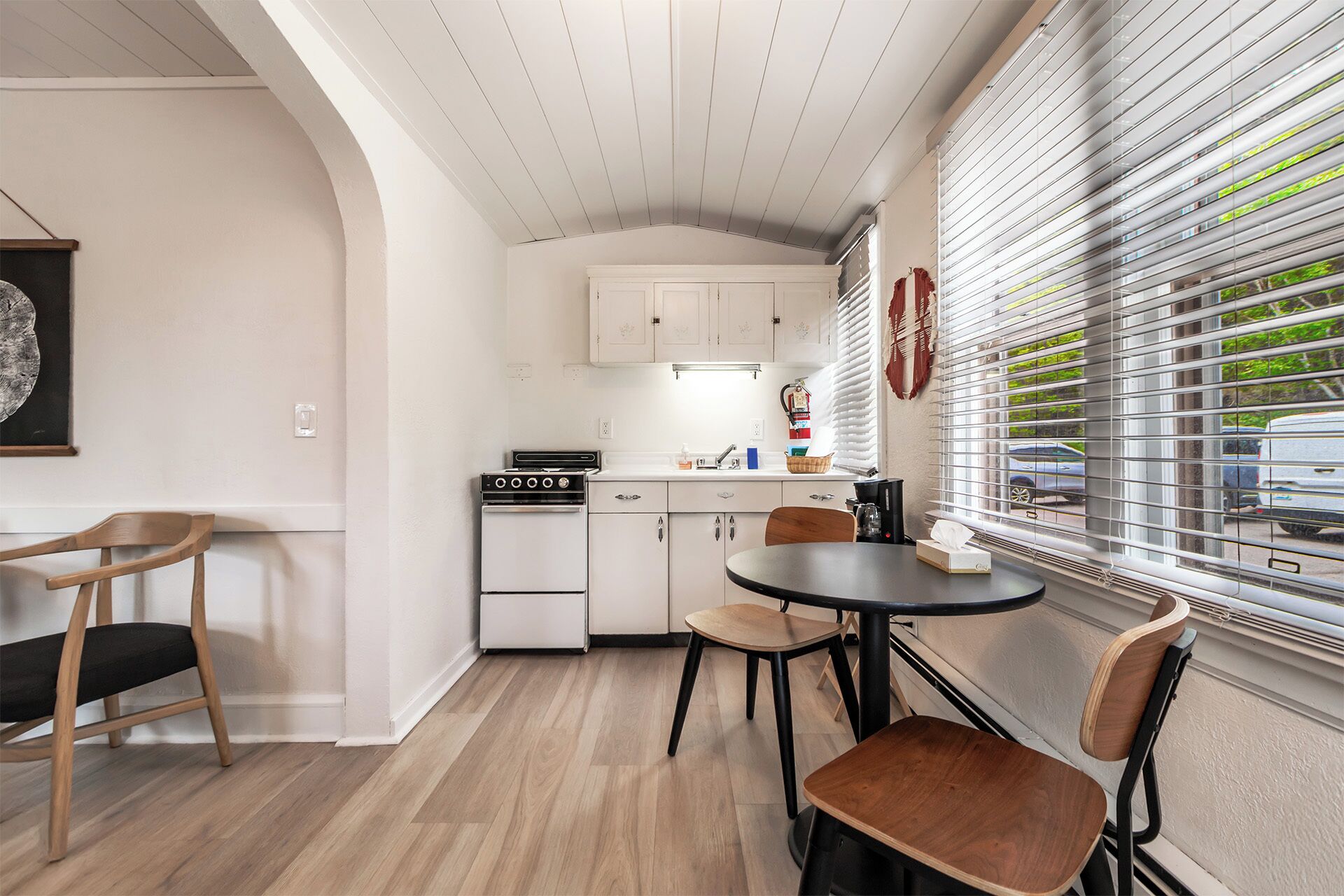 A compact kitchen with white cabinets, a stove, and a dining area with a round table and chairs.