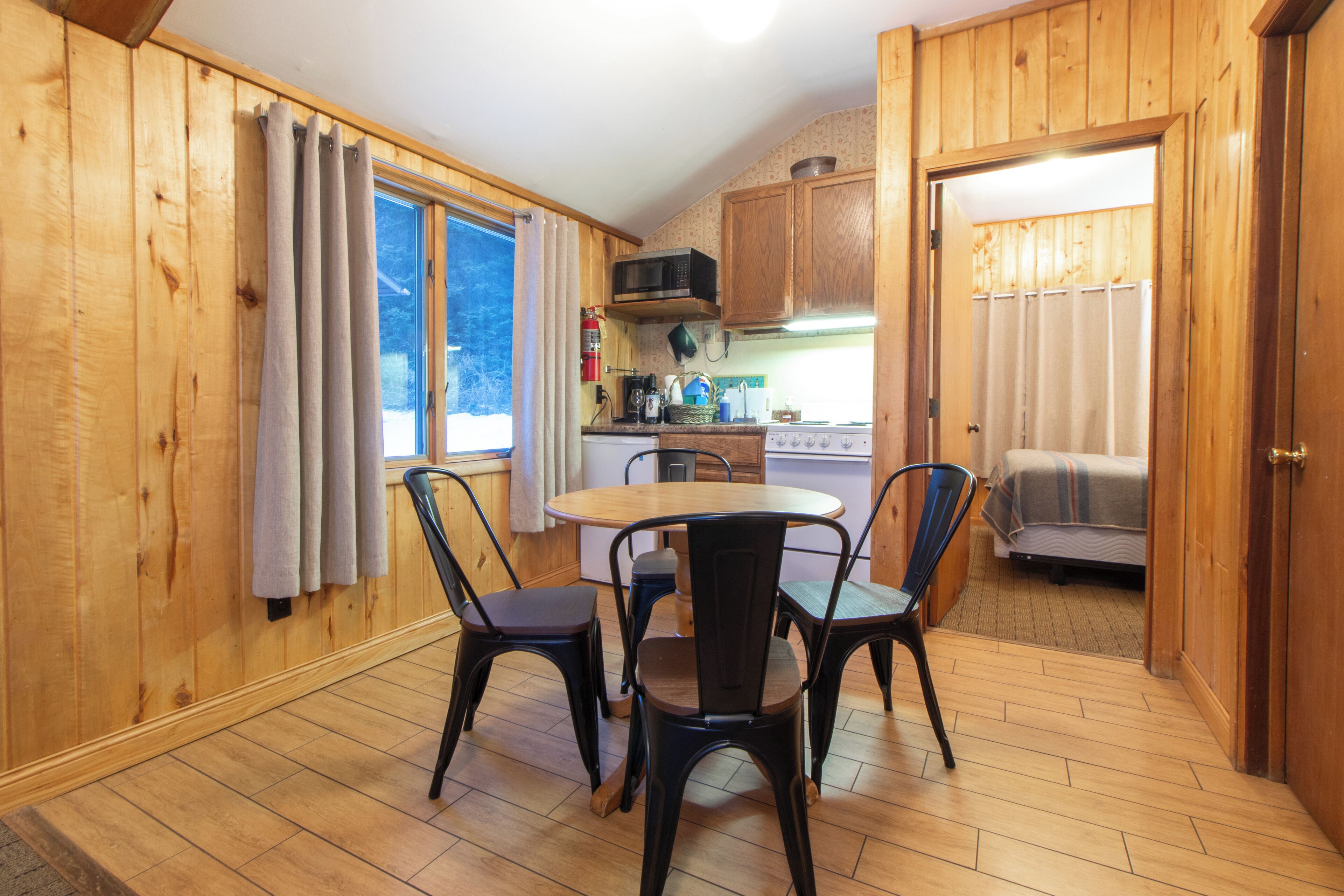 Une cuisine compacte aux murs en bois, une table à manger avec quatre chaises, un four à micro-ondes et une cuisinière.