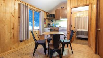 Una cocina compacta con paredes de madera, una mesa de comedor con cuatro sillas, un microondas y una estufa.