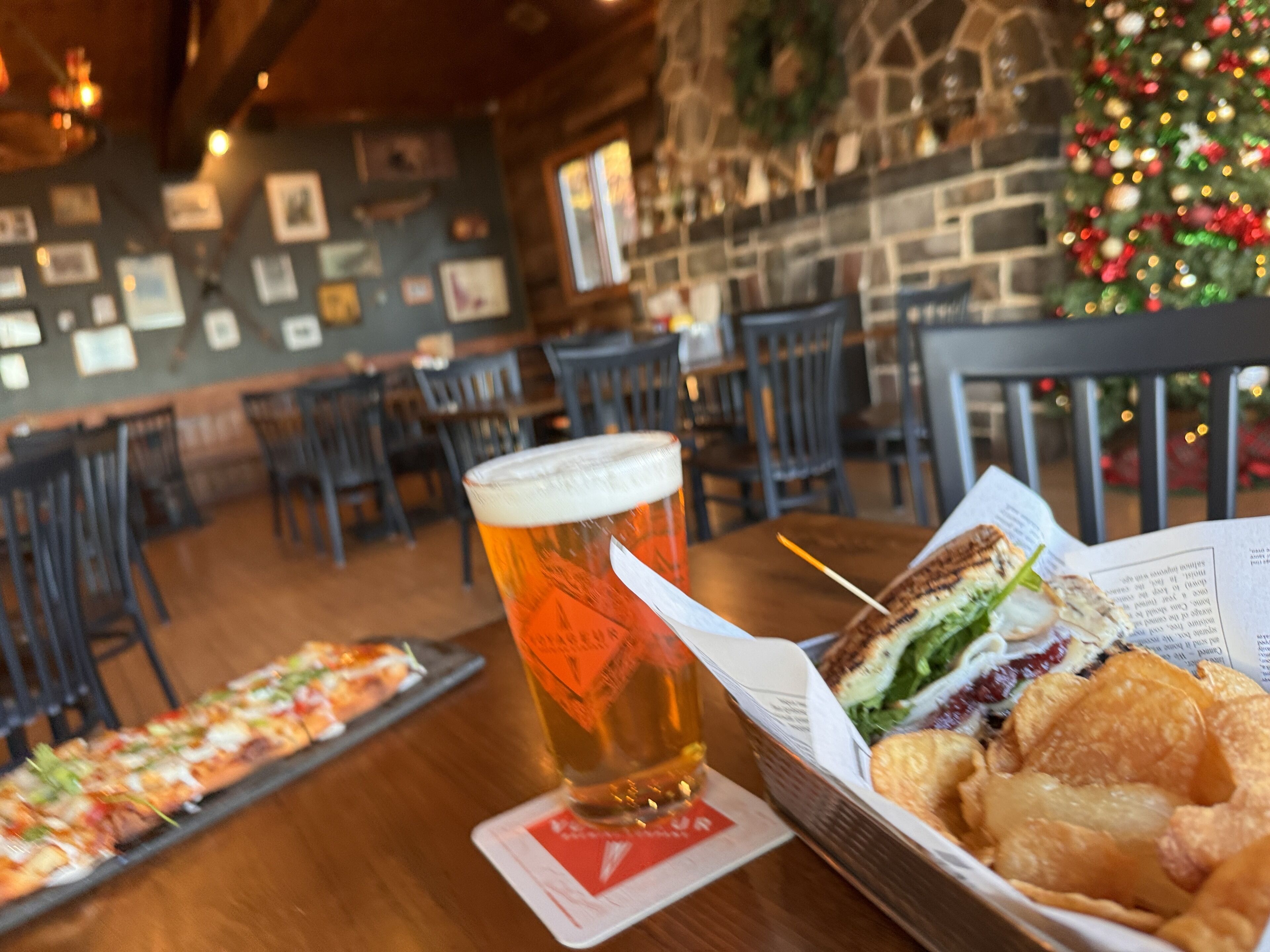 A dining table with a glass of beer, a sandwich, and a tray of food.