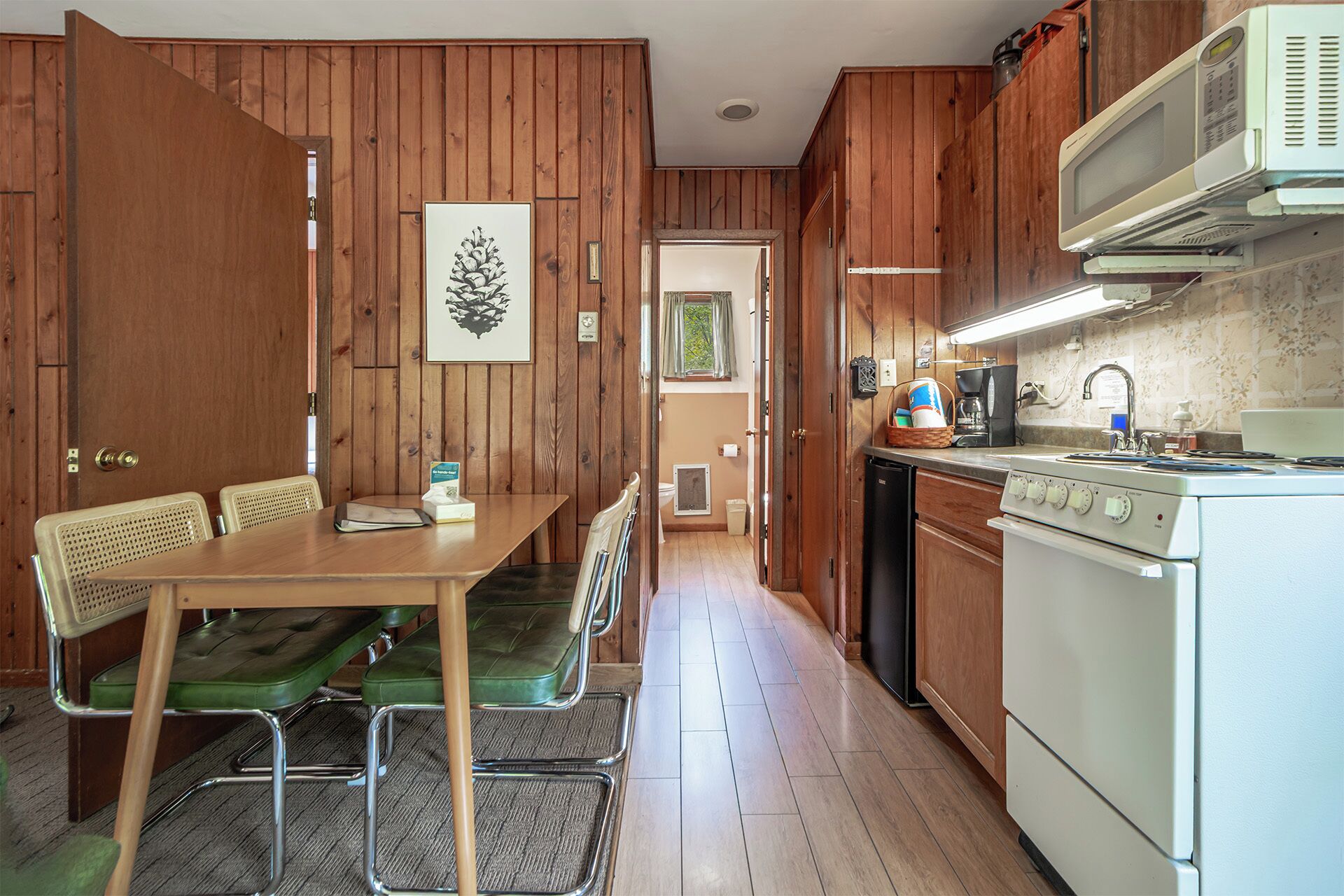 Een compacte keuken met houten kastjes, een eettafel met stoelen, een magnetron en een fornuis.