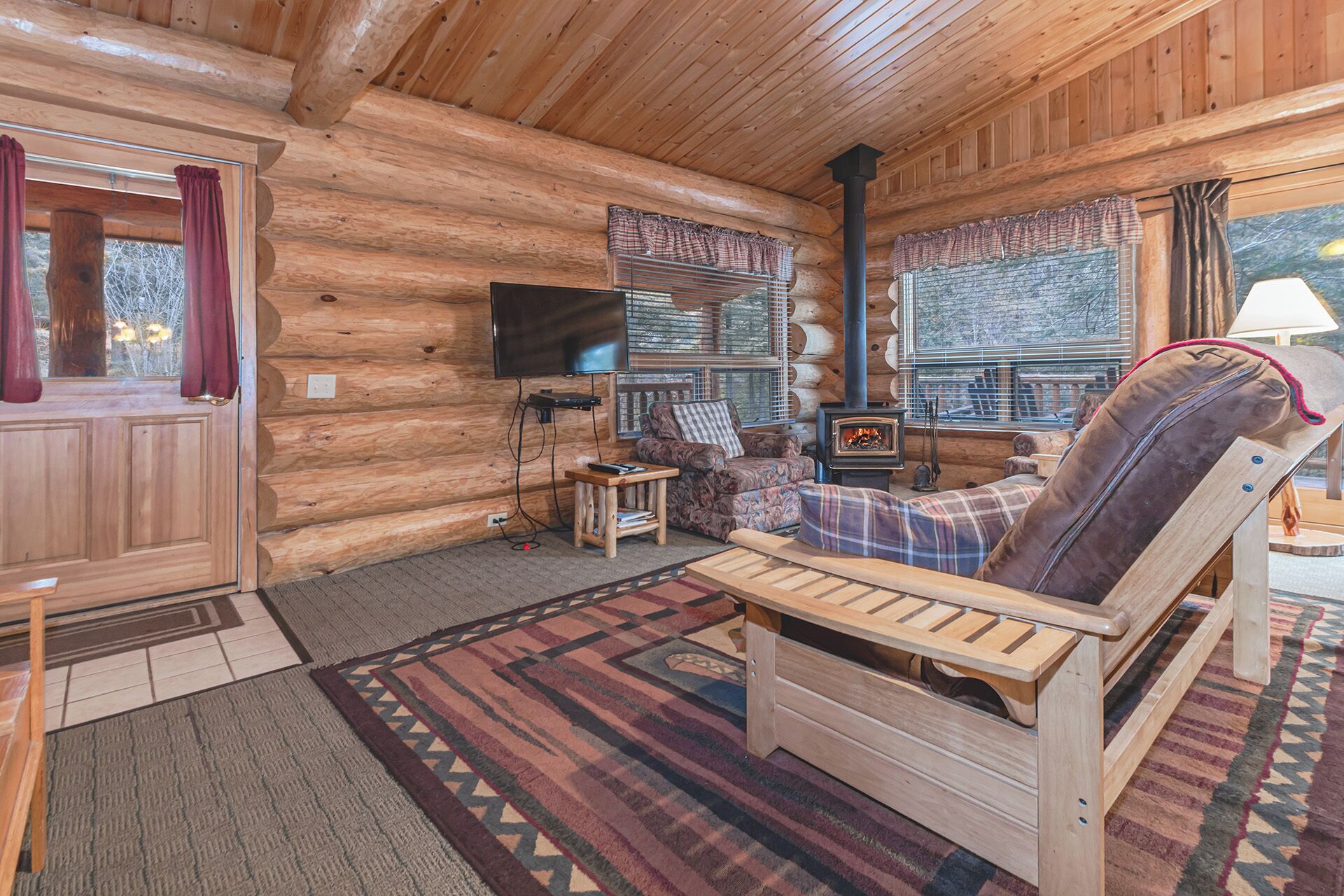 L’intérieur d’un chalet en bois chaleureux et accueillant, avec une cheminée, un téléviseur et un coin salon confortable.