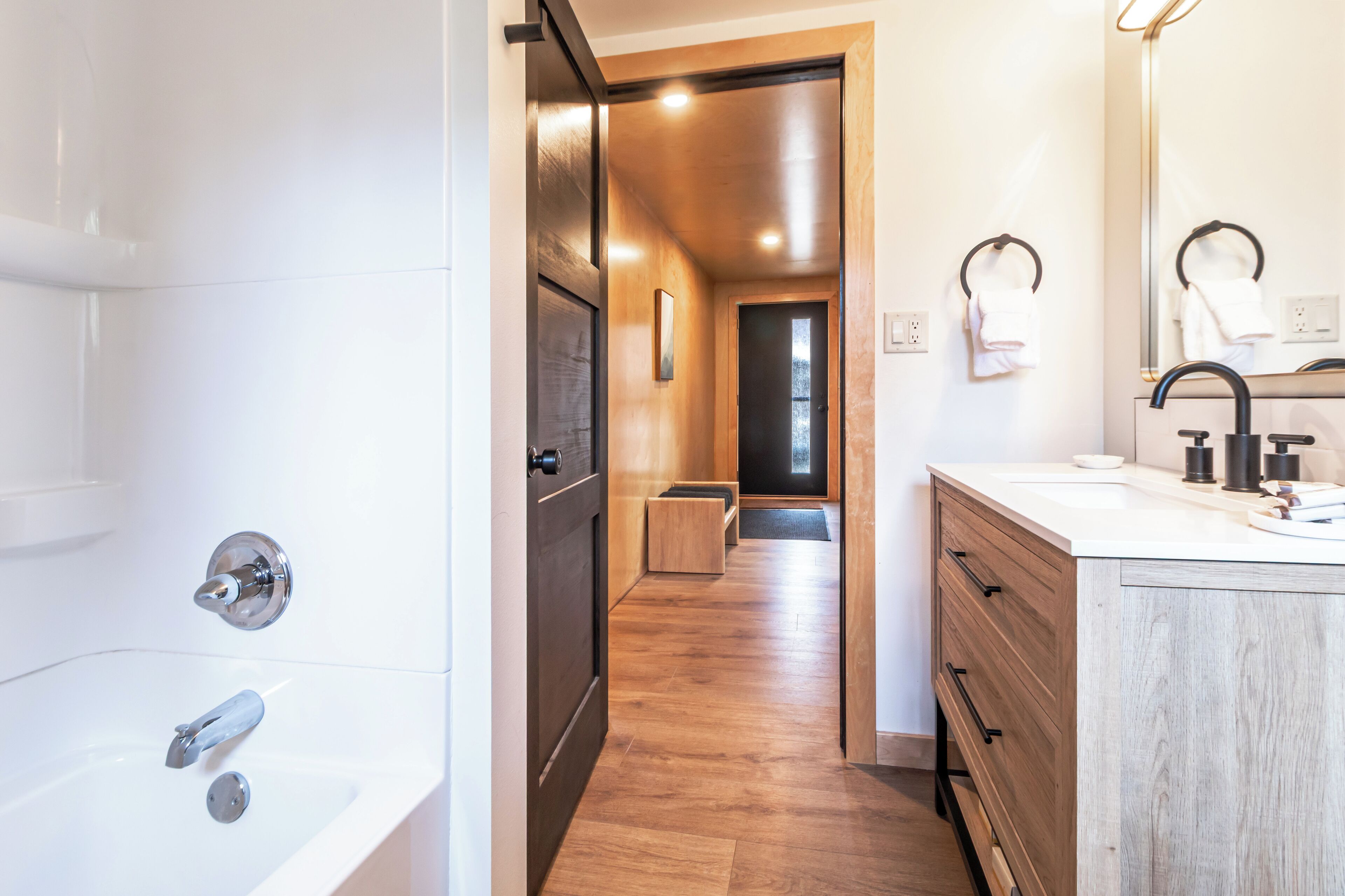 A modern bathroom with a wooden floor, a bathtub, a sink with a mirror, and a towel rack.