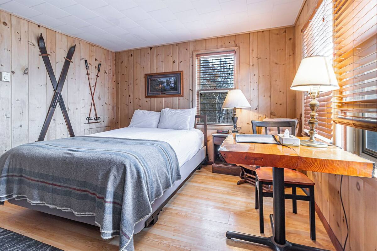 A cozy room with a bed, a desk, and skis leaning against the wall.