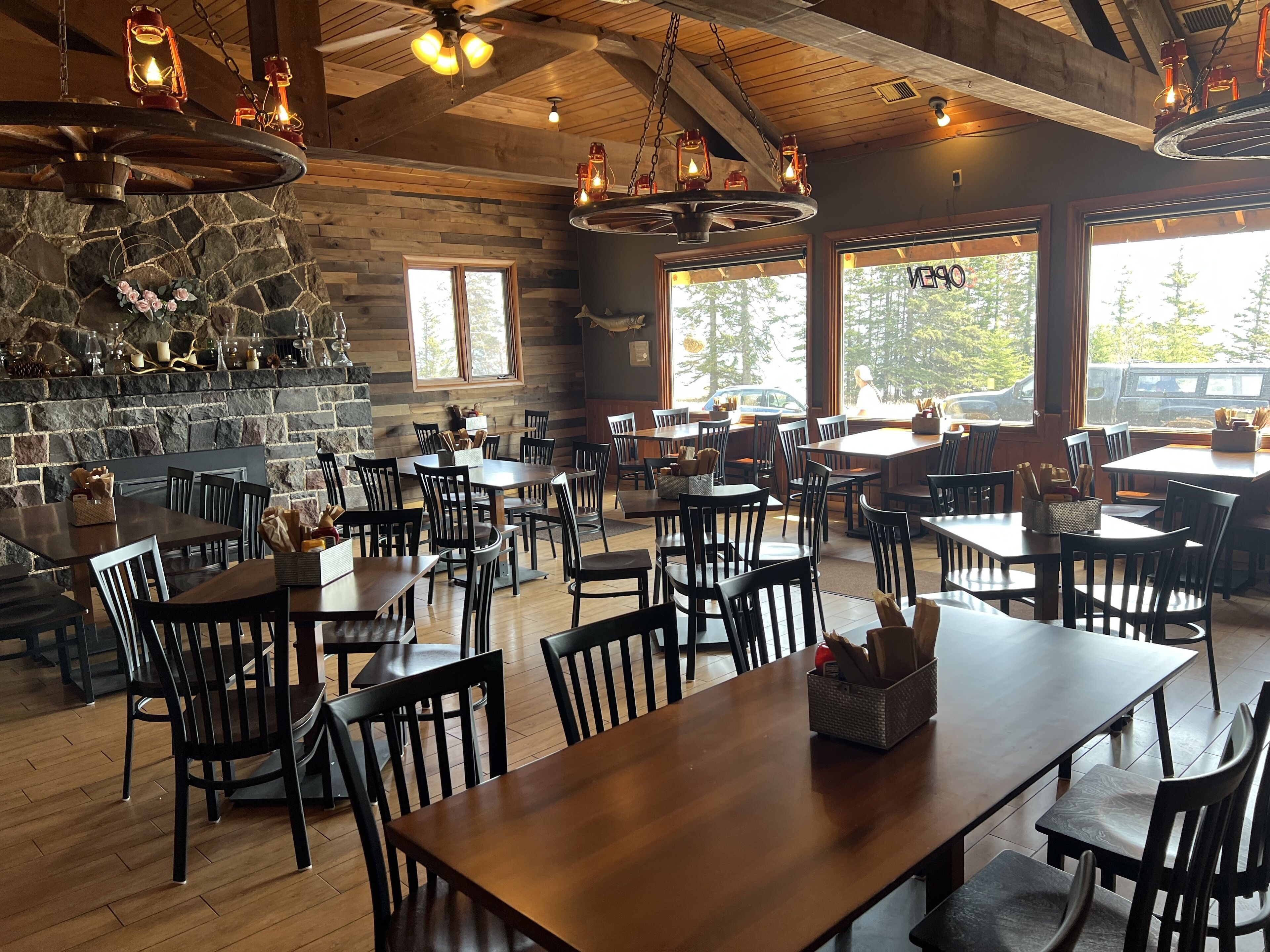 A restaurant with wooden tables and chairs, stone walls, and large windows.