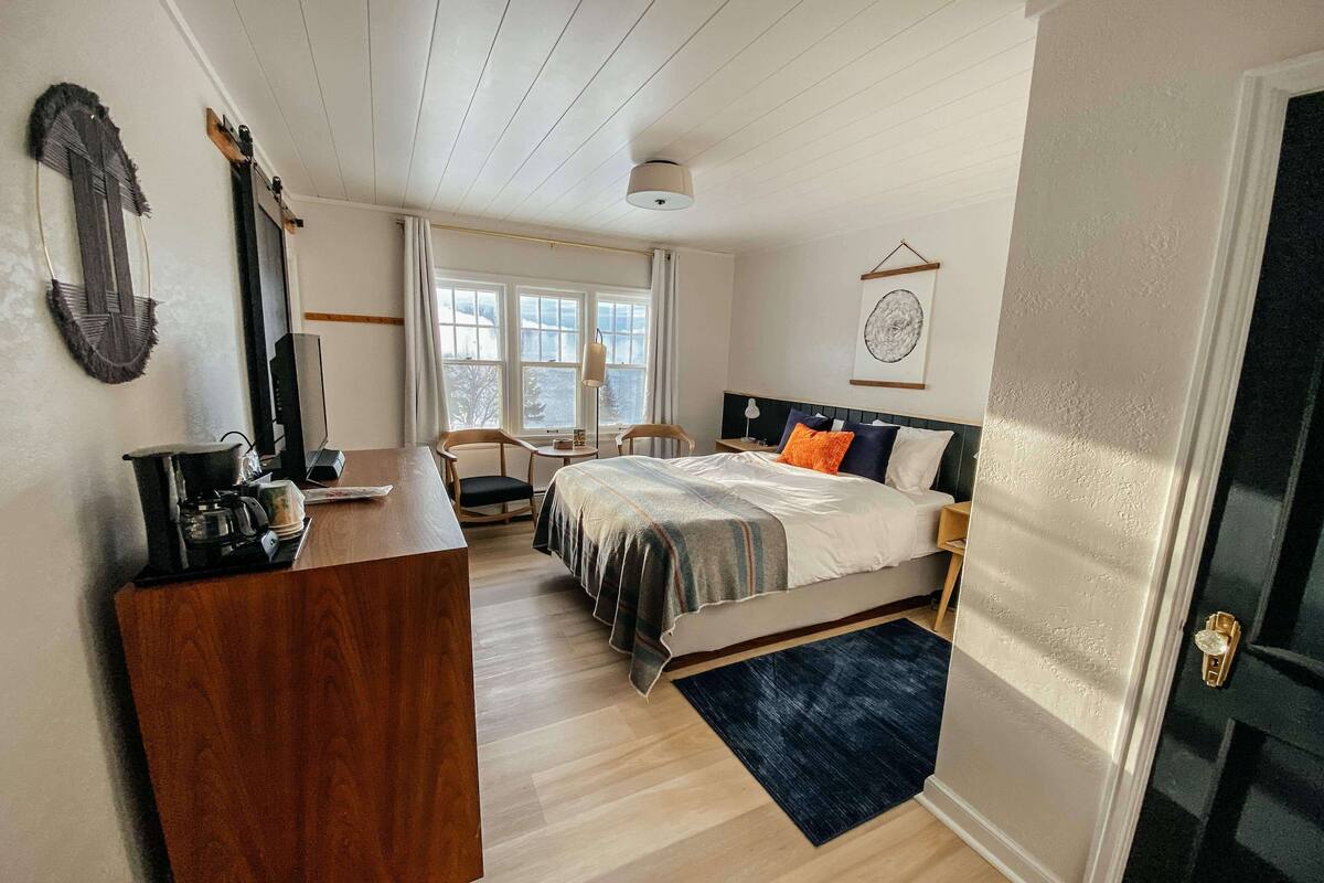 A bedroom with a bed, bedside tables, a desk, a chair, a window, and a door.