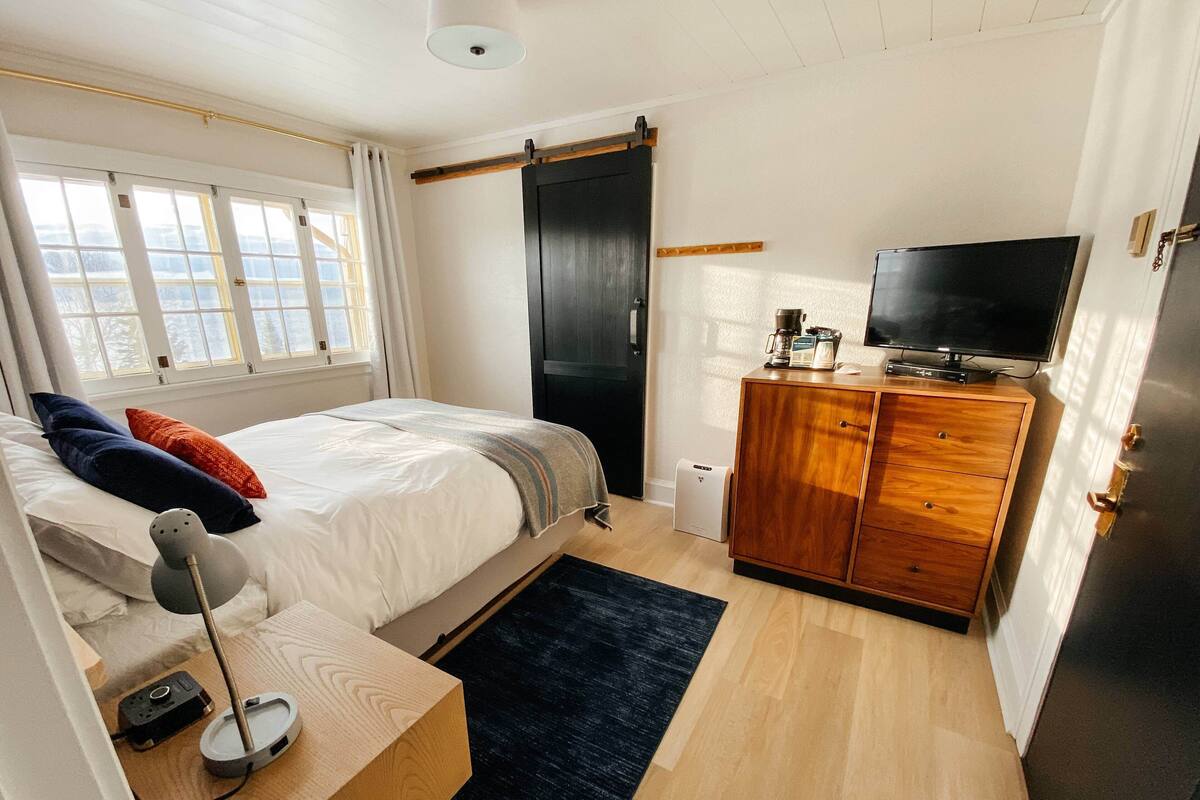 A bedroom with a bed, a dresser, a television, and a window with curtains.