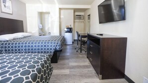 Una habitación de hotel con dos camas, un escritorio, una silla, un televisor de pantalla plana y una kitchenette.