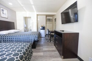 Una habitación de hotel con dos camas, un escritorio, una silla, un televisor de pantalla plana y una kitchenette.