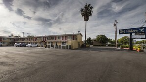 Un motel con estacionamiento, una palmera y un letrero que dice 'Sky Riders Motel'.
