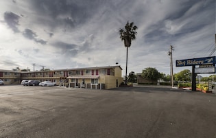 Un motel con estacionamiento, una palmera y un letrero que dice 'Sky Riders Motel'.
