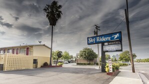 Un motel llamado 'Sky Riders' con un letrero, una palmera y un edificio de fachada amarilla.