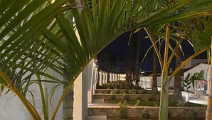 A well-lit outdoor area with a stone staircase leading to a higher level, surrounded by greenery and palm trees. - Relaxia Los Girasoles (San Bartolomé de Tirajana)