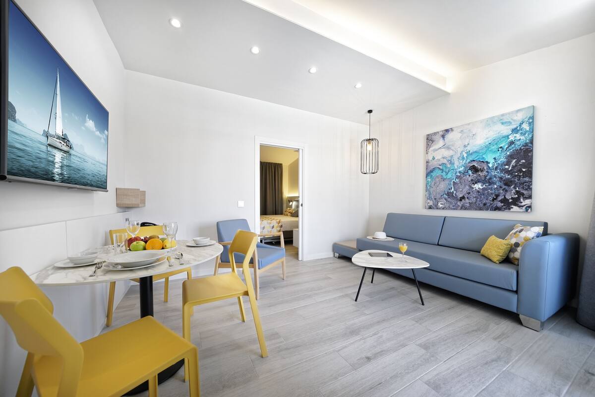 A modern living room with a dining area, a sofa, and a painting on the wall.