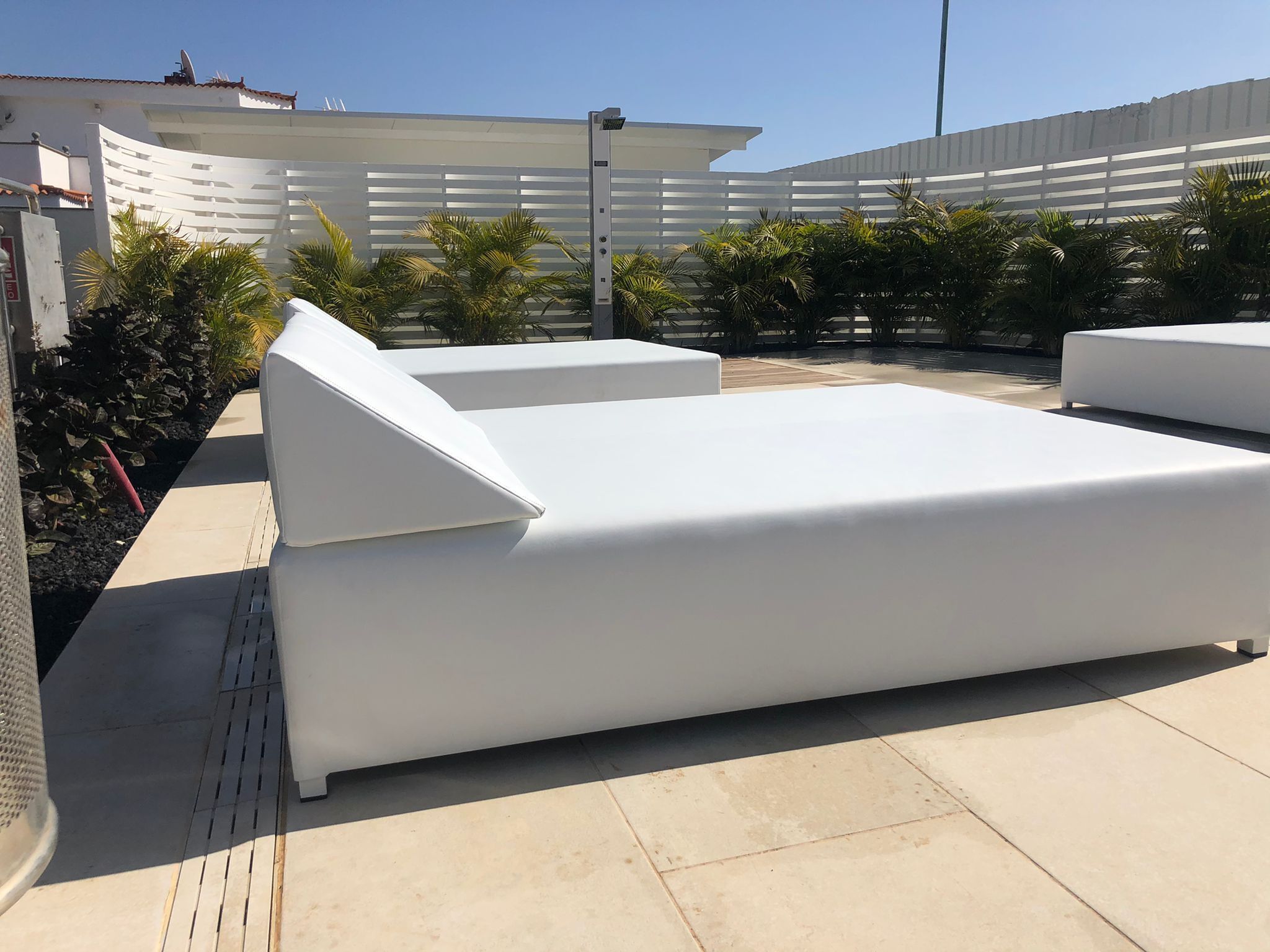 Un espacio moderno para sentarse al aire libre con sillas reclinables blancas y una superficie plana, rodeado por una cerca blanca y follaje.