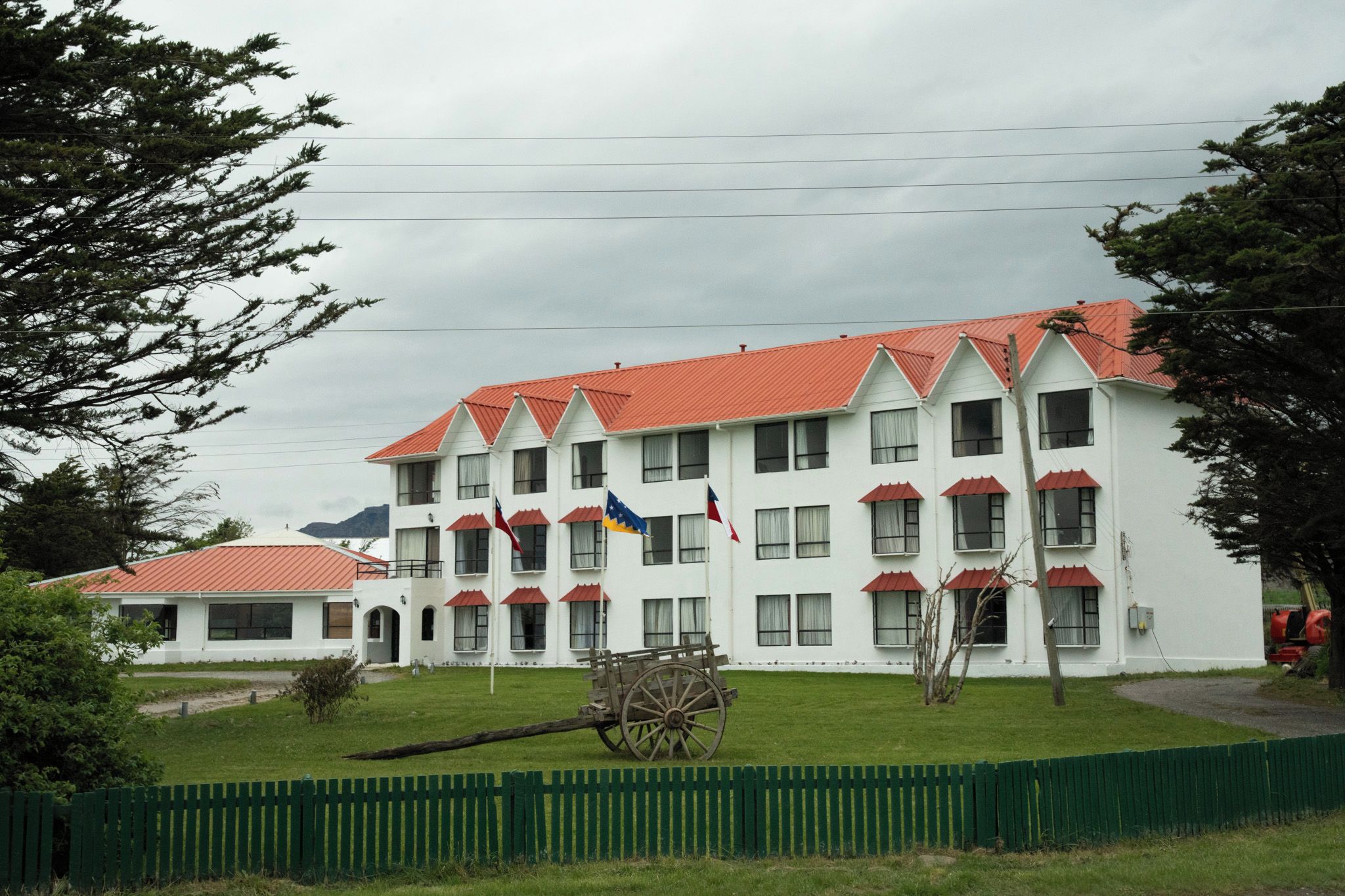 A multi-story building with a red roof, several flags, and a wooden cart in the foreground.