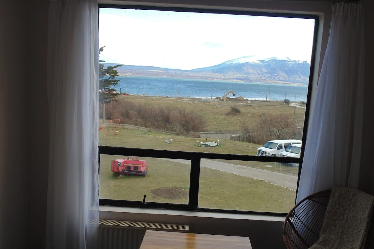 A room with a large window offering a view of a lake, a distant mountain, and a construction site.