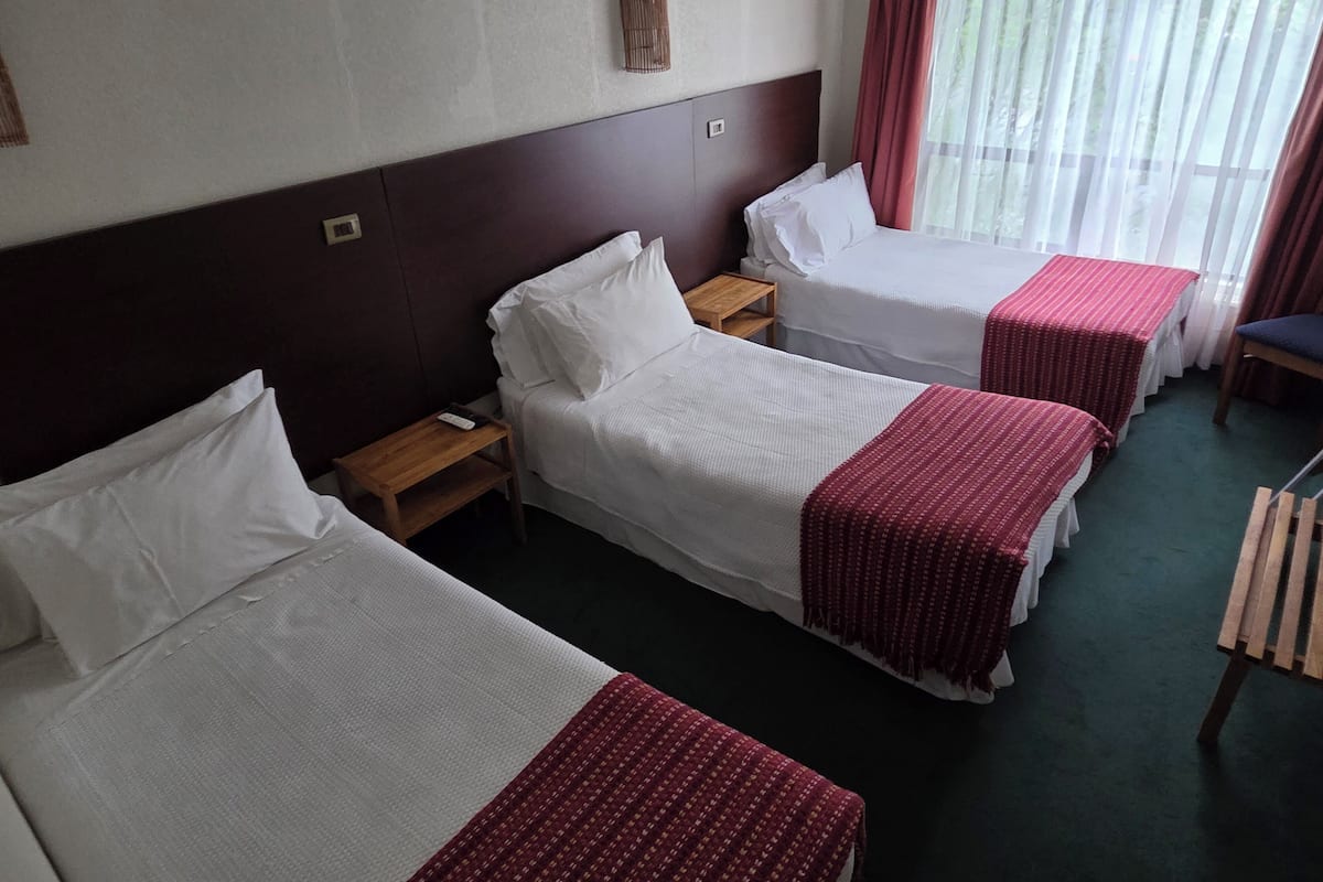 A hotel room with two single beds, a wooden nightstand, a small table, and a chair.