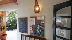 A reception area with a wooden bench, a wall-mounted bulletin board with various notices, a hanging light fixture, and a door with a caution sign. - Hotel HD Natales (Natales)