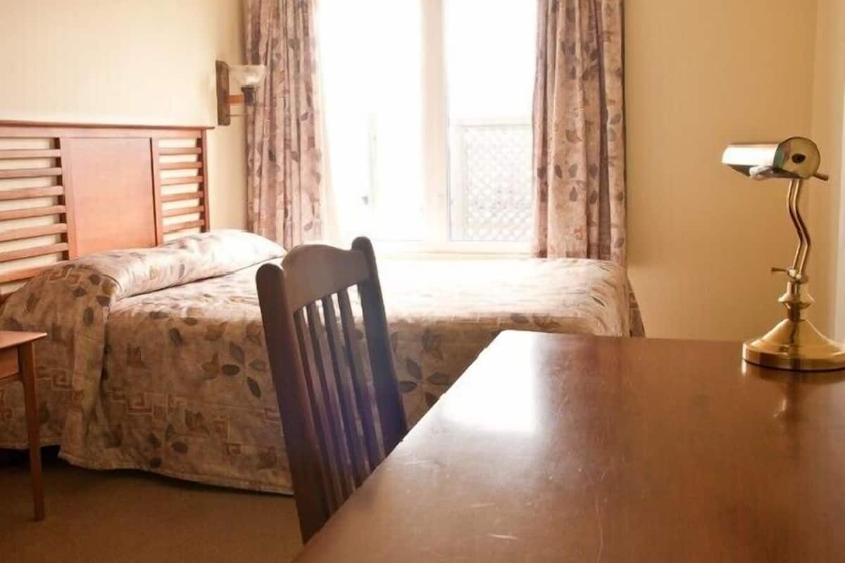 A room with a wooden bed, a wooden chair, a table, and a lamp.