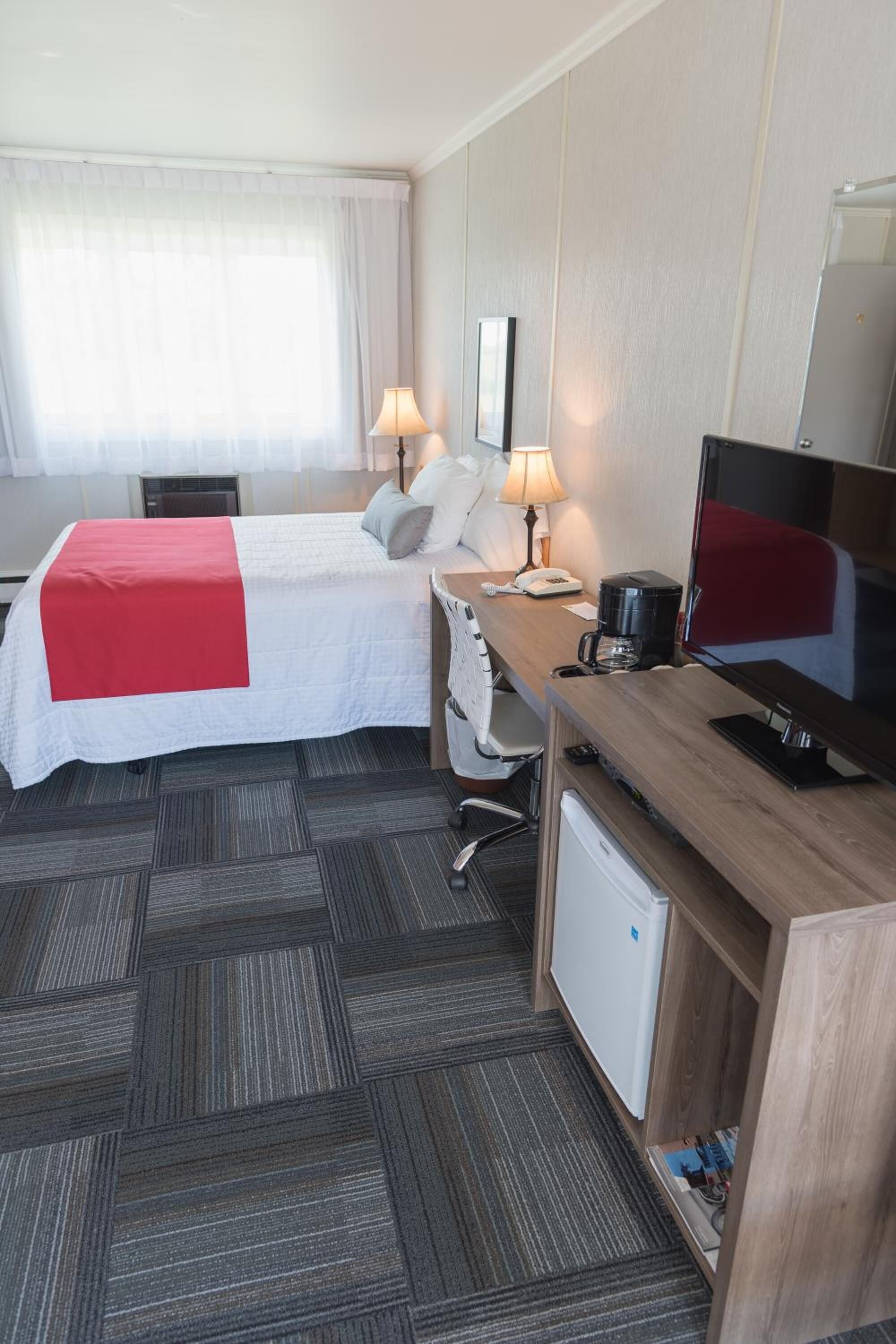 A hotel room with a bed, desk, chair, television, and a small refrigerator.