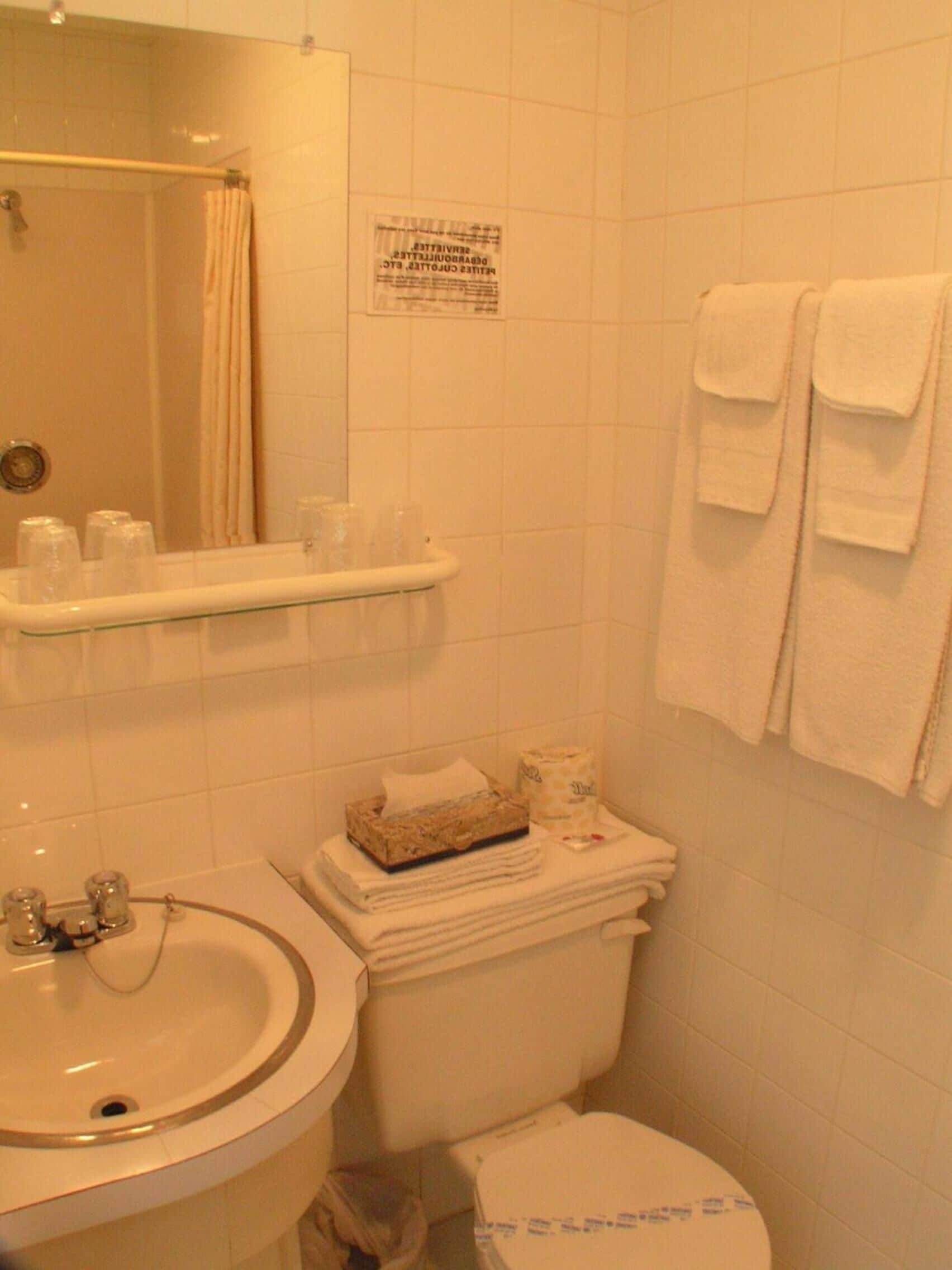 A bathroom with a sink, toilet, and a mirror. There are towels hanging on the wall and a shelf with toiletries.