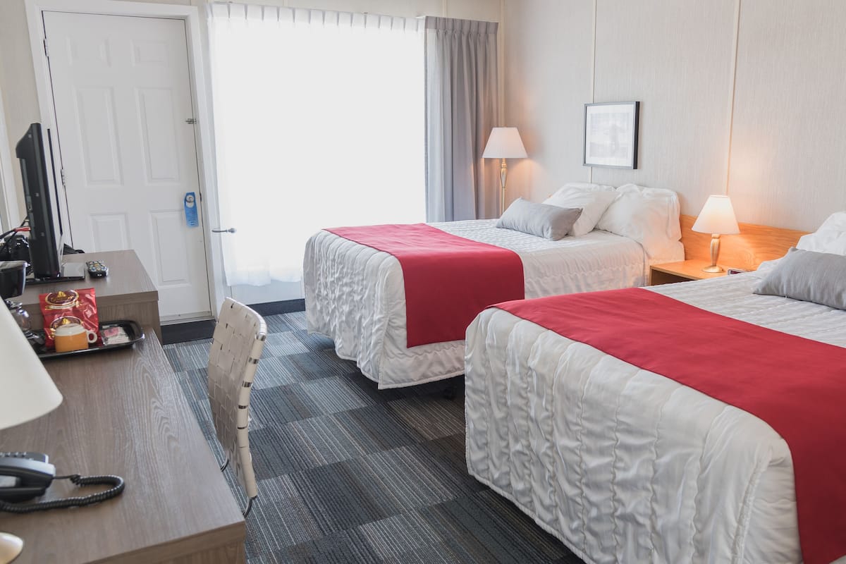 A hotel room with two beds, a desk, a chair, a lamp, and a framed picture on the wall.