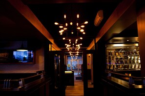 A dimly lit bar area with a long counter, a television mounted on the wall, and a display of bottles on shelves. - Motel Cartier (Rivière-du-Loup)